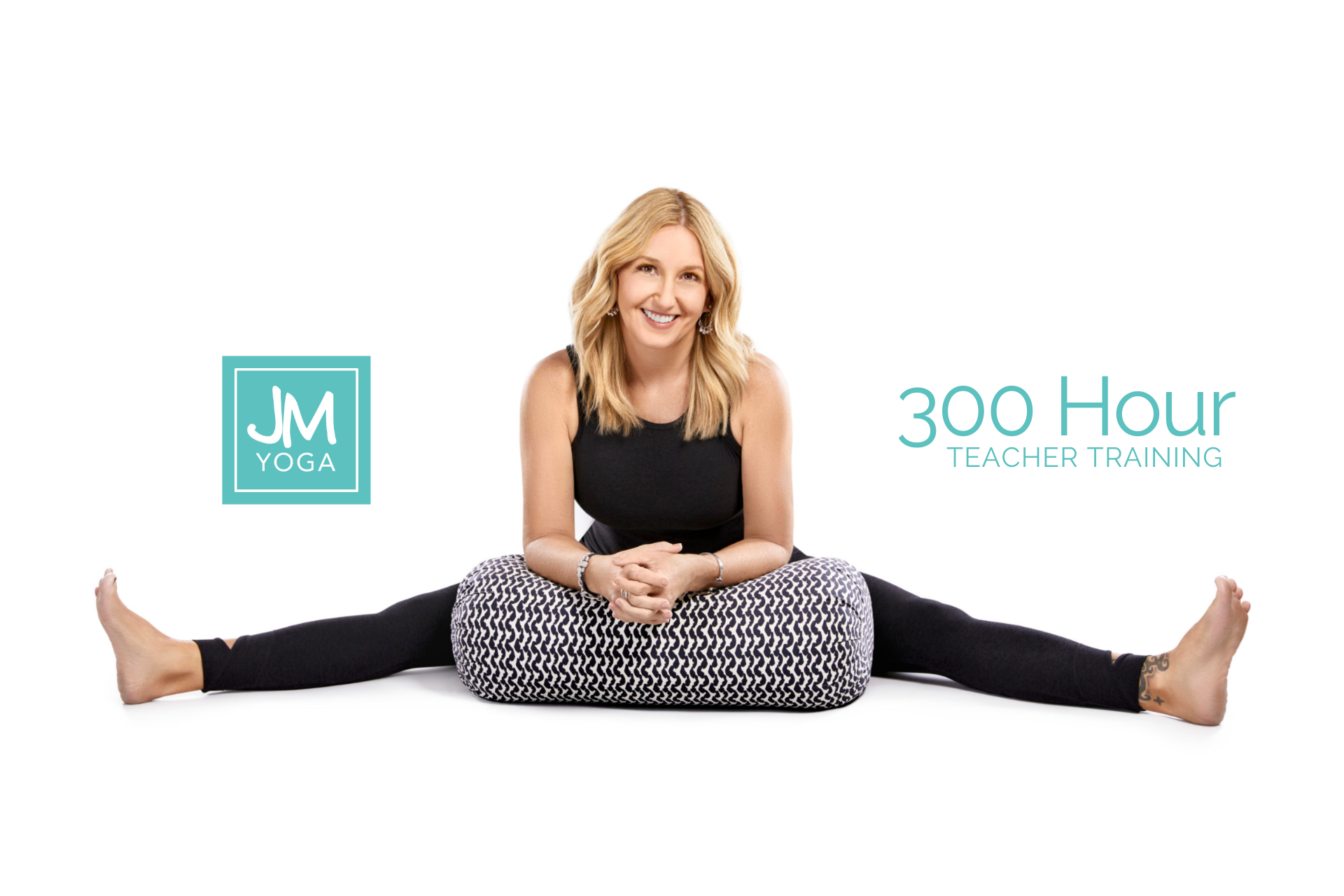 Jules is wearing black sitting in a wide leg forward fold resting her elbows on a black and white bolster against a white background. The words "300 hr yoga teacher training" are in green against the white background.